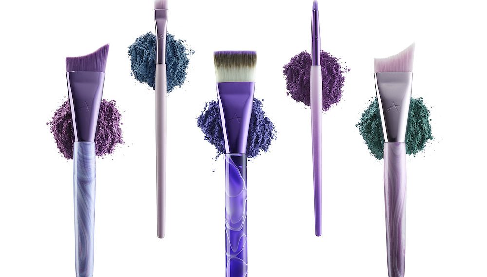Five cosmetic brushes from Anisa Internationals "Spiral Fusion" brush set, each brush set upon it's own loose pile of cosmetic powders.